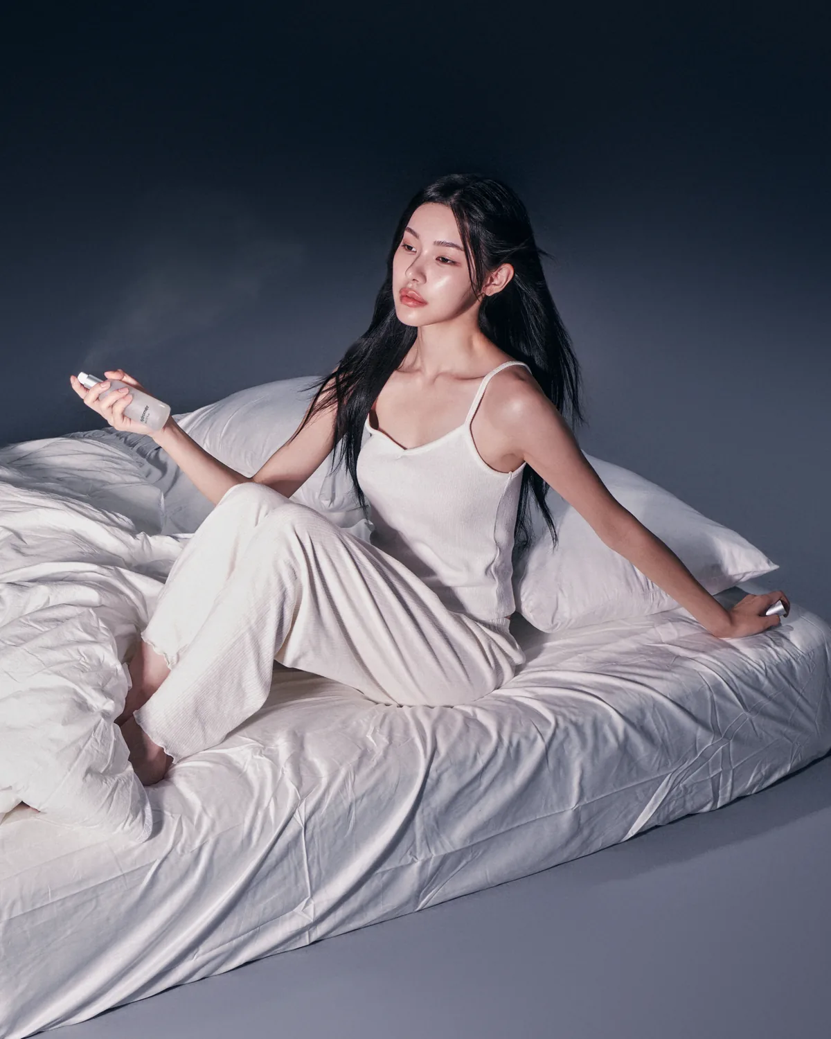 Model in white on white bedding spraying Hydromer treatment mist